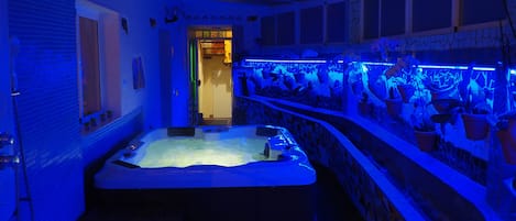 Un cuarto de spa con hidromasaje, una silla de masaje montada en la pared y una fila de plantas en macetas.