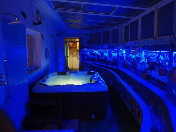 A spa room with a hot tub, a wall-mounted massage chair, and a row of potted plants.