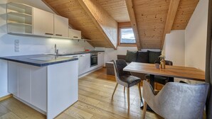 A modern kitchen with white cabinets, a wooden ceiling, and a dining area with a table and chairs. - Luxury Apartment "Weißhorn" with Mountain View and private Steam Sauna (Deutschnofen)