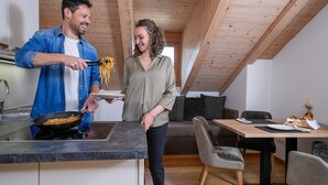 A modern kitchen with wooden beams, a dining area with a table and chairs, and a sofa. - Luxury Apartment "Weißhorn" with Mountain View and private Steam Sauna (Deutschnofen)