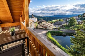 Ein Holzbalkon mit Blick auf ein Dorf, einen Teich und Berge im Hintergrund.