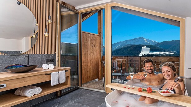 A modern bathroom with a large bathtub, wooden vanity, and a view of a mountain landscape.