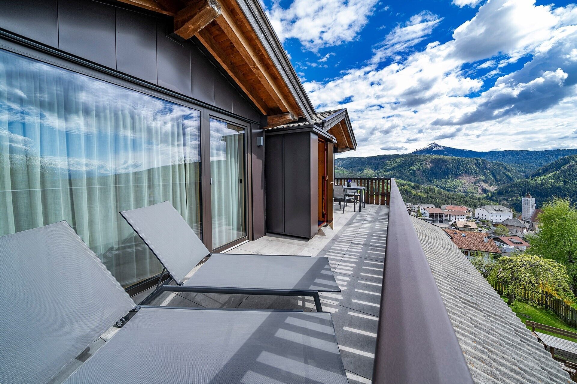 A balcony with two lounge chairs, a sliding glass door, and a view of a mountain range.
