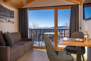 A cozy room with a wooden ceiling, a sofa, a dining table with chairs, and a view of snow-capped mountains.