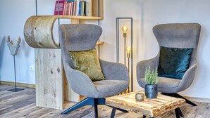 Two grey armchairs with cushions, a wooden coffee table, a bookshelf with books, and a decorative wooden sculpture.