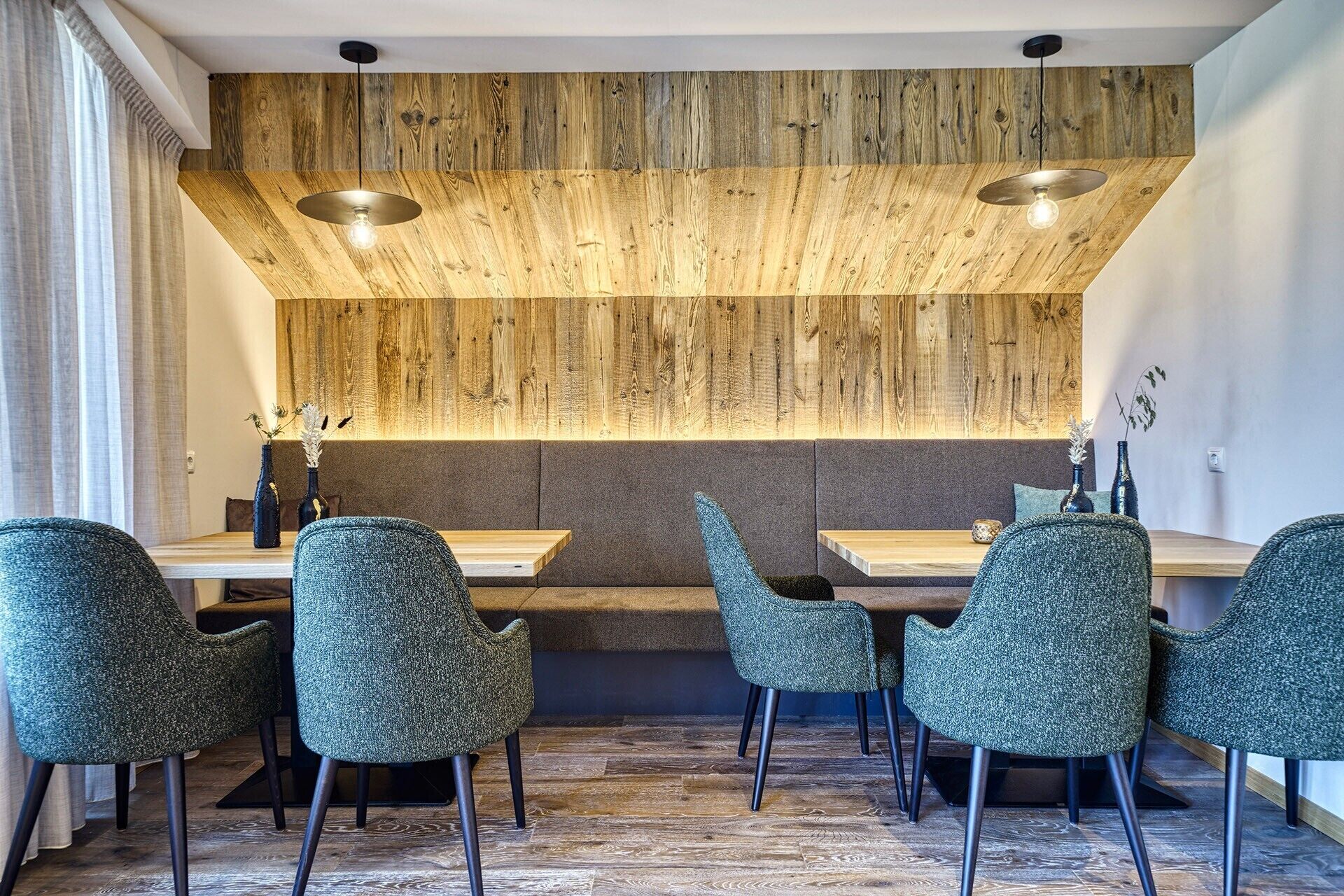 Un comedor con paredes de paneles de madera, dos lámparas colgantes y seis sillas tapizadas en verde.