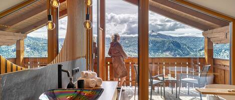 A wooden cabin with a large window, a bathroom with a sink, and a view of mountains.