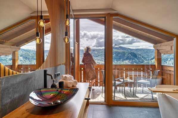 A wooden cabin with a large window, a bathroom with a sink, and a view of mountains. - Apartment "Schwarzhorn": Mountain View, Infrared Sauna and Feestanding Bathtub (Deutschnofen)