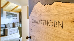 A wooden door with 'SCHWARZHORN' carved into it, a living room with a sofa and a painting, and a wooden ceiling.