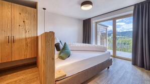 A bedroom with a bed, wooden wardrobe, and a view through a large window. - Apartment "Schlossberg  Rosengarten" with Mountain View, Private Finnish Sauna & Garden (Deutschnofen)