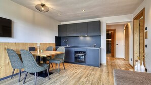 A modern kitchen with dark cabinetry, a built-in oven, and a dining area with a wooden table and grey upholstered chairs. - Apartment "Schlossberg  Rosengarten" with Mountain View, Private Finnish Sauna & Garden (Deutschnofen)