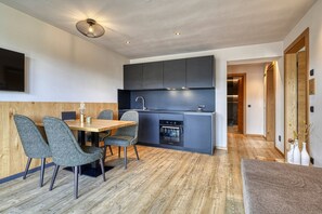 Een moderne keuken met donkere kastjes, een ingebouwde oven en een eethoek met een houten tafel en grijze fauteuils.