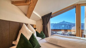 A bedroom with a wooden headboard, a large window with a mountain view, and a balcony with outdoor seating. - "Schlern" with Mountain View, Whirlpool, Finnish Sauna & Steam Sauna & Balcony (Deutschnofen)