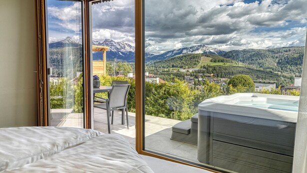 Ein Schlafzimmer mit großem Fenster, einem Bett, einem Tisch mit Stuhl und einer Whirlwanne.