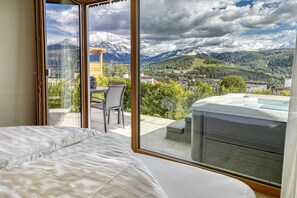 Un dormitorio con un ventanal grande, una cama, una mesa con una silla y un jacuzzi.