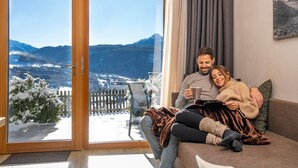 Ein Paar sitzt auf einer Couch und blickt durch eine Glasdoor auf die Berge.