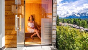 Eine Holzsauna mit Glastür, einer hölzernen Sitzbank und Blick auf Berge und Häuser.