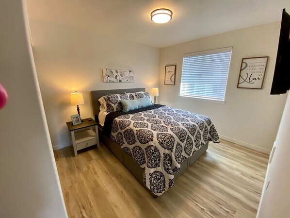 Une chambre à coucher avec un lit, des lampes de chevet, une table de chevet, une fenêtre avec des stores et un luminaire au plafond.
