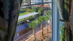 Blick durch ein Fenster mit Vorhängen auf einen Fluss, eine Fußgängerbrücke und Gebäude im Hintergrund.