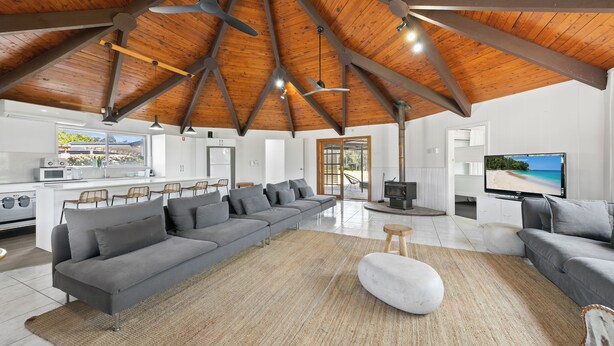 Un salón espacioso con un amplio sofá seccional gris, un otoman blanco y una cocina al fondo.