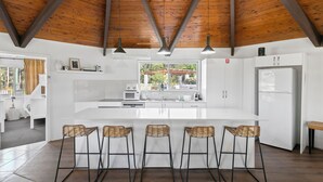 Una cocina moderna con una isla grande, armarios blancos y techo de madera.