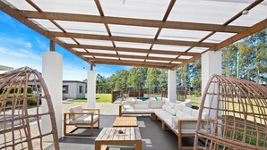 Un patio al aire libre con una mesa de madera, sofás blancos y sillas de mimbre.