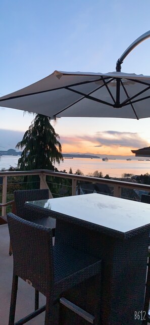 Enjoy a serene view of the water from this outdoor seating area with a table and chairs under a shaded umbrella.