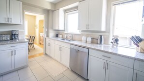 A modern kitchen with white cabinets, stainless steel appliances, and a large window providing natural light. - Beach house- Stunning Ocean & City Views | West Van Retreat (West Vancouver)