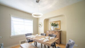 A dining area with a wooden table, cushioned chairs, a bench, and a chandelier. - Beach house- Stunning Ocean & City Views | West Van Retreat (West Vancouver)