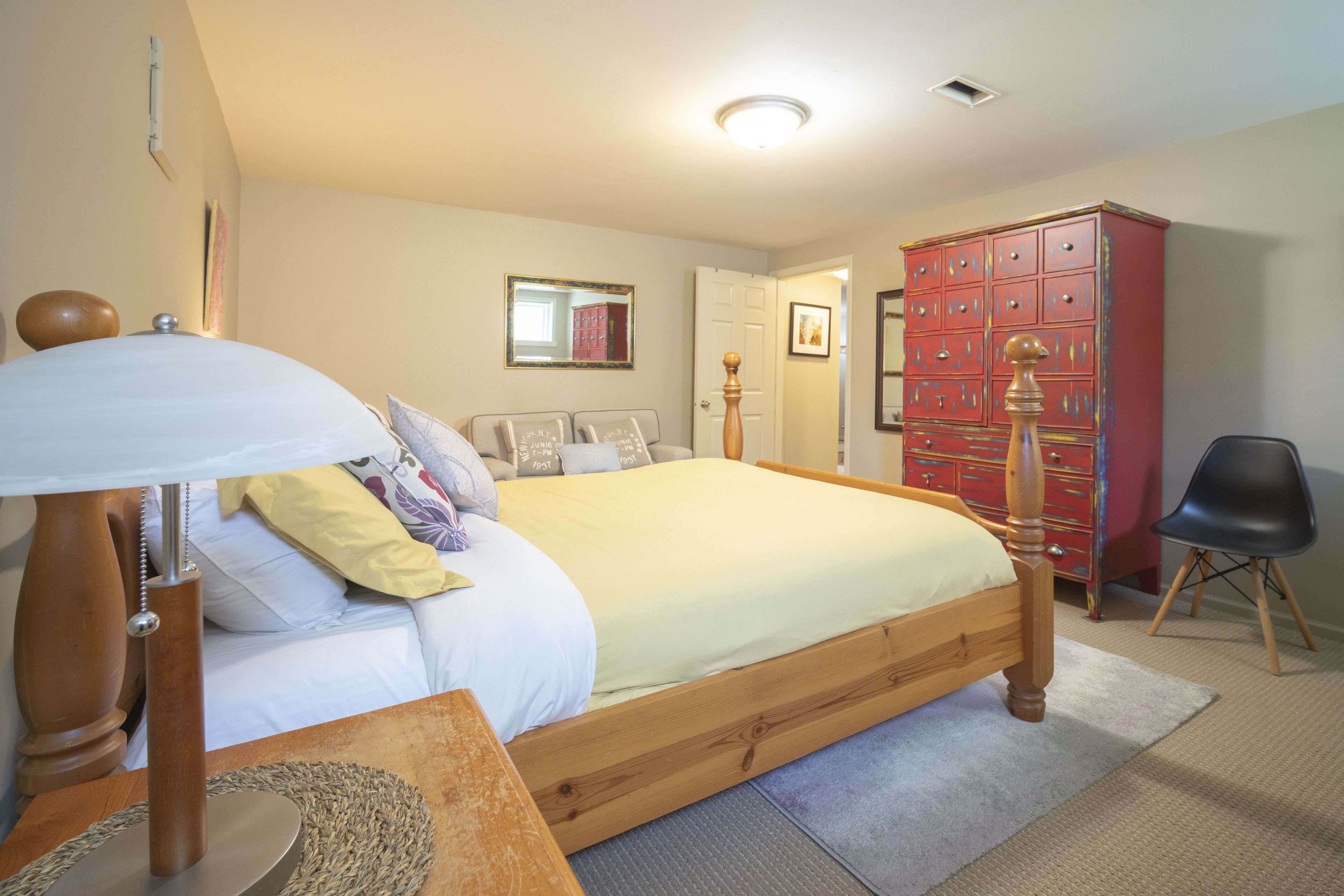 A bedroom with a wooden bed, a bedside table with a lamp, a wardrobe, and a chair.