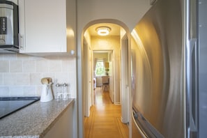 Stylish hallway leads to a well-equipped kitchen with a modern stove, refrigerator, and coffee maker.