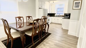 Een moderne keuken met witte kasten, een houten eettafel met stoelen en een zwart tapijt.