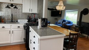 A kitchen with white cabinets, a granite countertop, and a dining area with a blue sofa and wooden table. - Block Island The Way It Used To Be!!!  Steps From Everything!!! (New Shoreham)