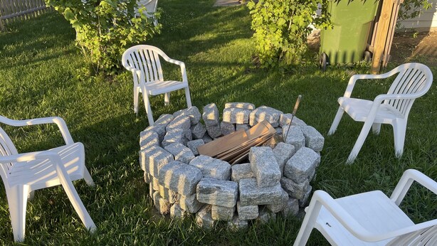 A stone fire pit surrounded by white plastic chairs in a grassy backyard. - Block Island The Way It Used To Be!!!  Steps From Everything!!! (New Shoreham)
