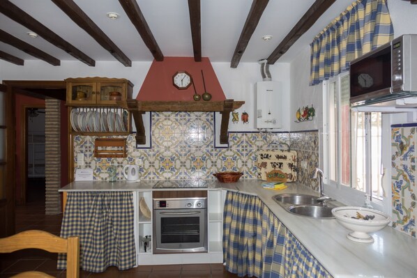Cozinha com painel de azulejos, armários de madeira, forno embutido e janela com cortinas.