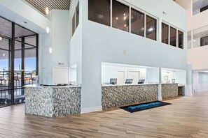 Un hall d’hôtel moderne avec un comptoir d’accueil, un balcon au deuxième étage et une vue sur le parking.