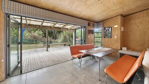 Un interior modern amb sostre de fusta, una porta de vidre que dona a l'exterior, una terrassa de fusta i una taula amb cadires.