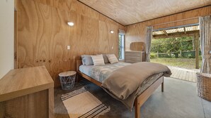 Una habitació amb sostre i parets de fusta, un llit amb estriatges, una taula rodona petita i una cistella de vimet.