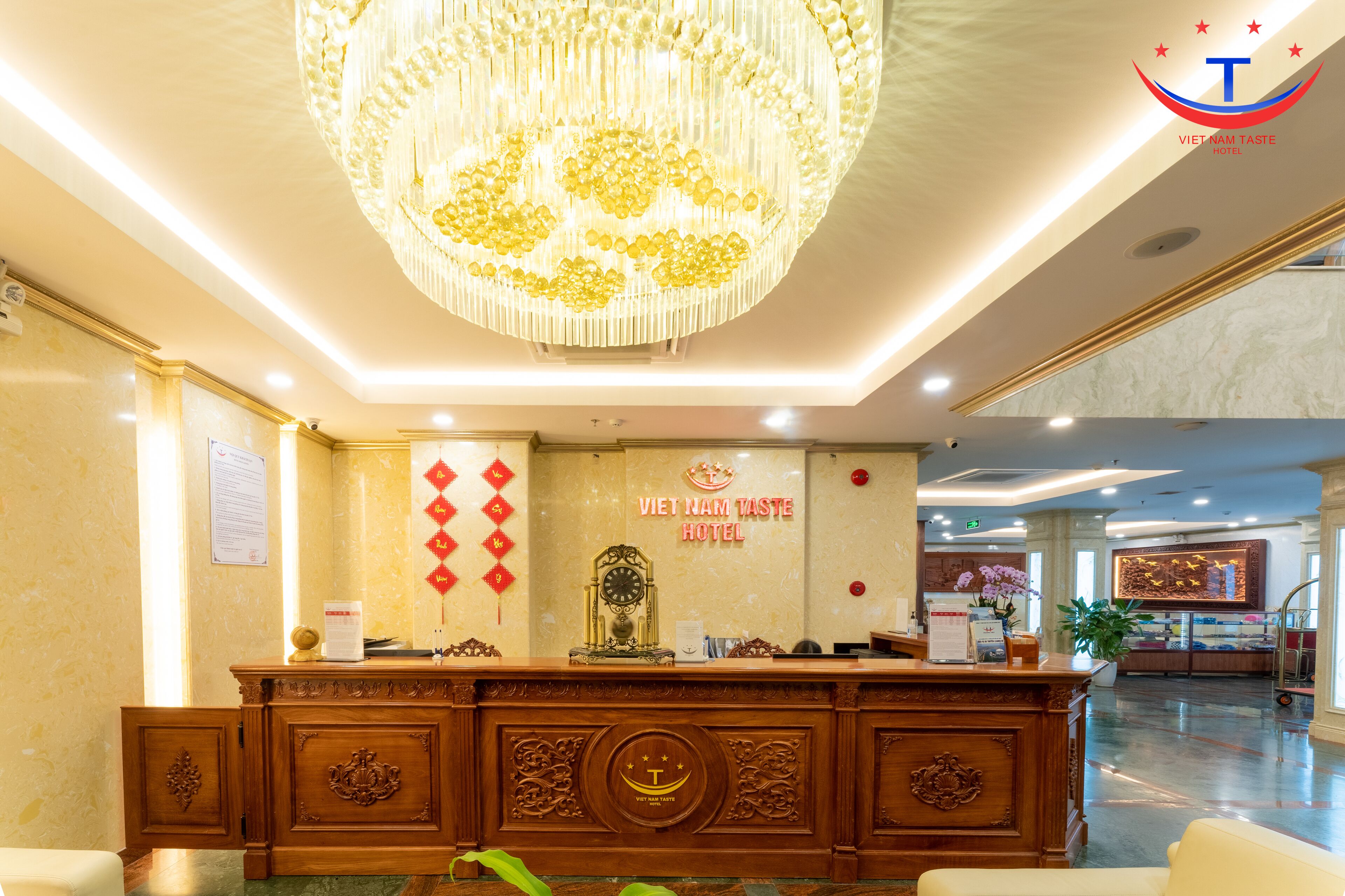 Zona de recepción de un hotel con una araña, un reloj y un cartel que indica Vietnam Taste Hotel.