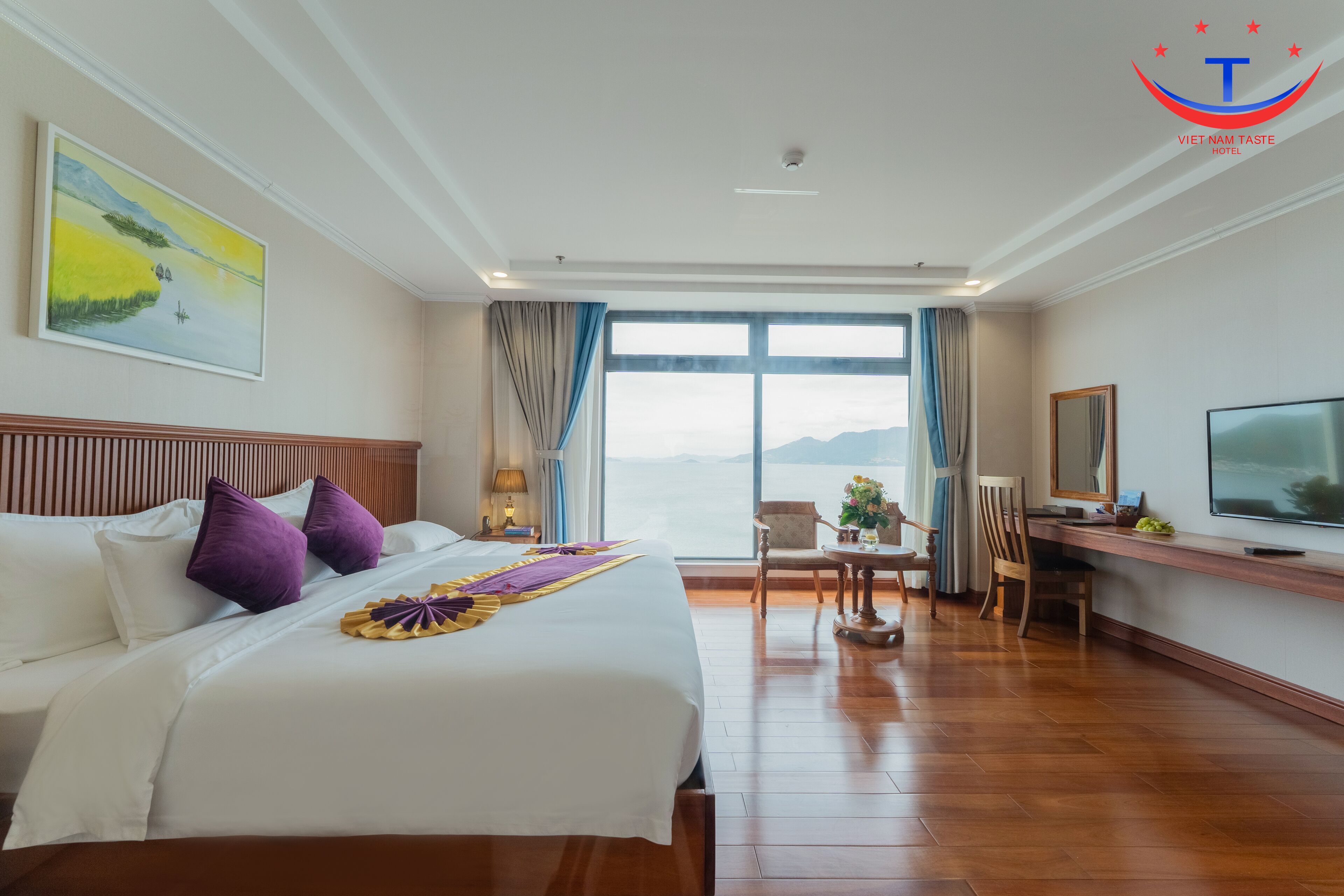 A hotel room with a large bed, a desk with a chair, a television, and a window with a view of the mountains.