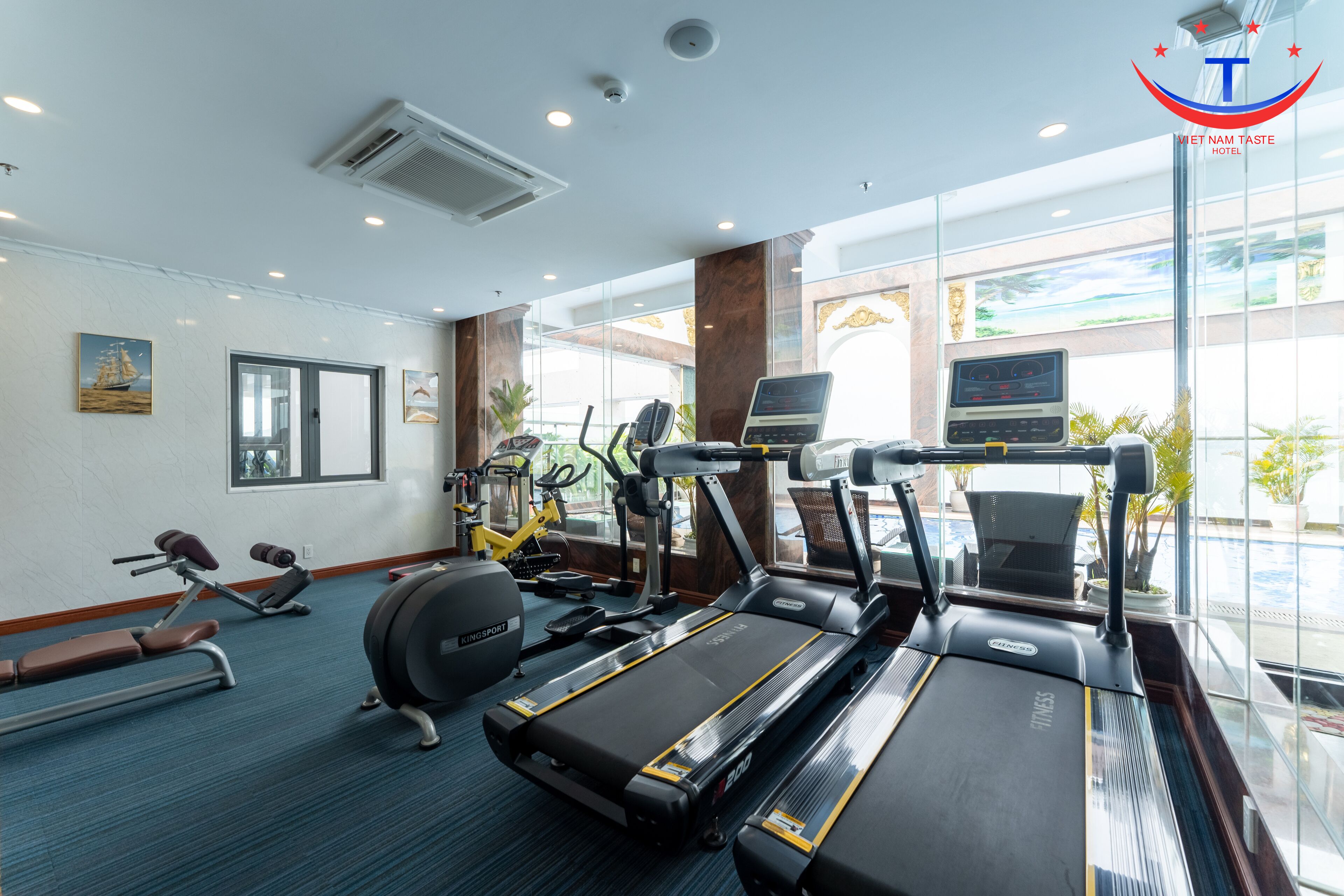 A hotel gym with treadmills, elliptical machines, and weight benches.