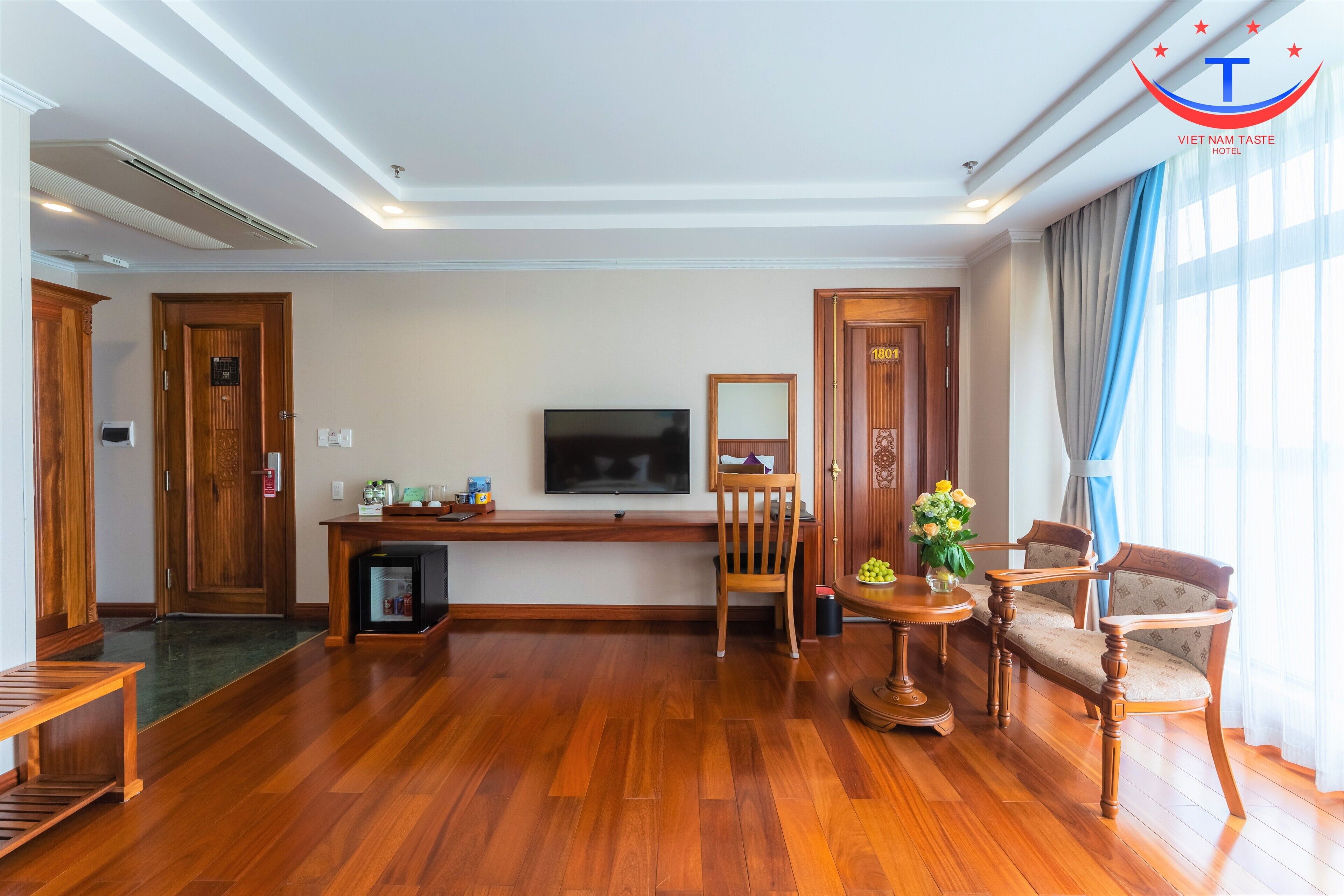 A spacious living room with wooden flooring, a flat-screen TV, a wooden coffee table, and two upholstered chairs.