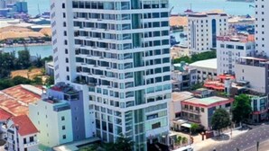 A high-rise hotel with multiple floors, a parking area, and a road with vehicles. - Vietnam Taste Hotel Quy Nhon - Beachfront (Quy Nhon)