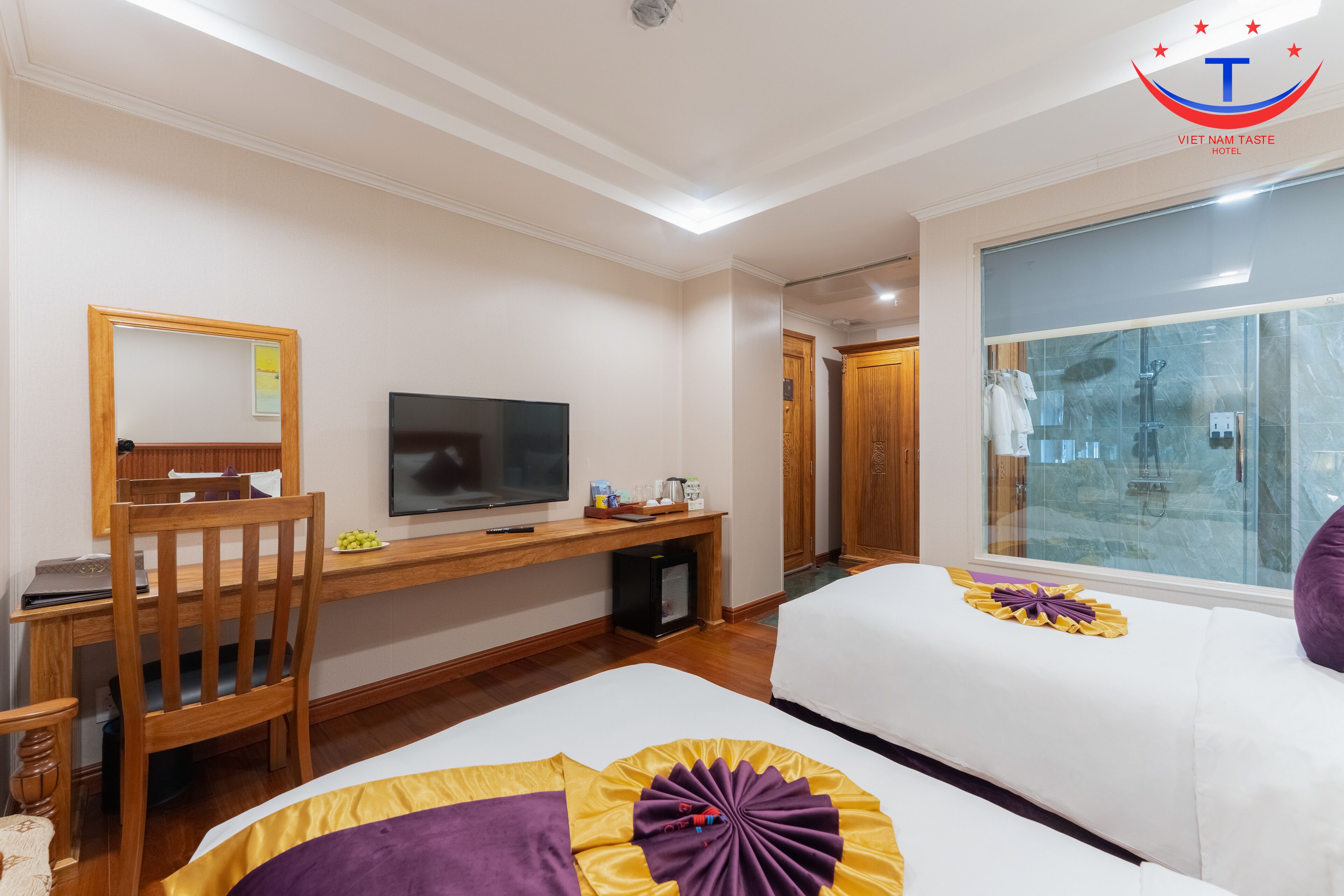 Una habitación de hotel con cama, escritorio con televisor, silla y baño con ducha de vidrio.