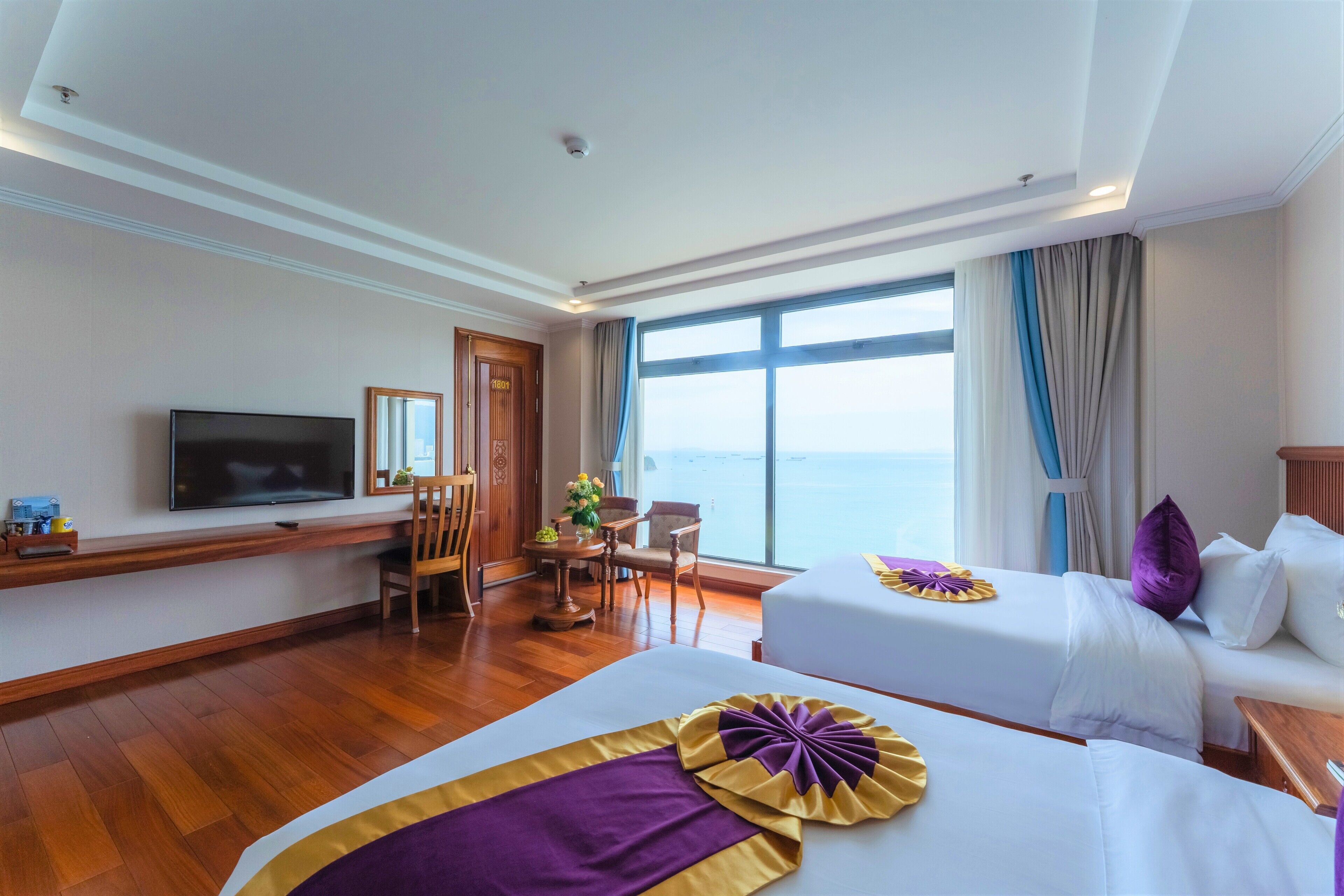 Camera d'albergo con due letti, televisione, scrivania e un'ampia finestra vista mare.