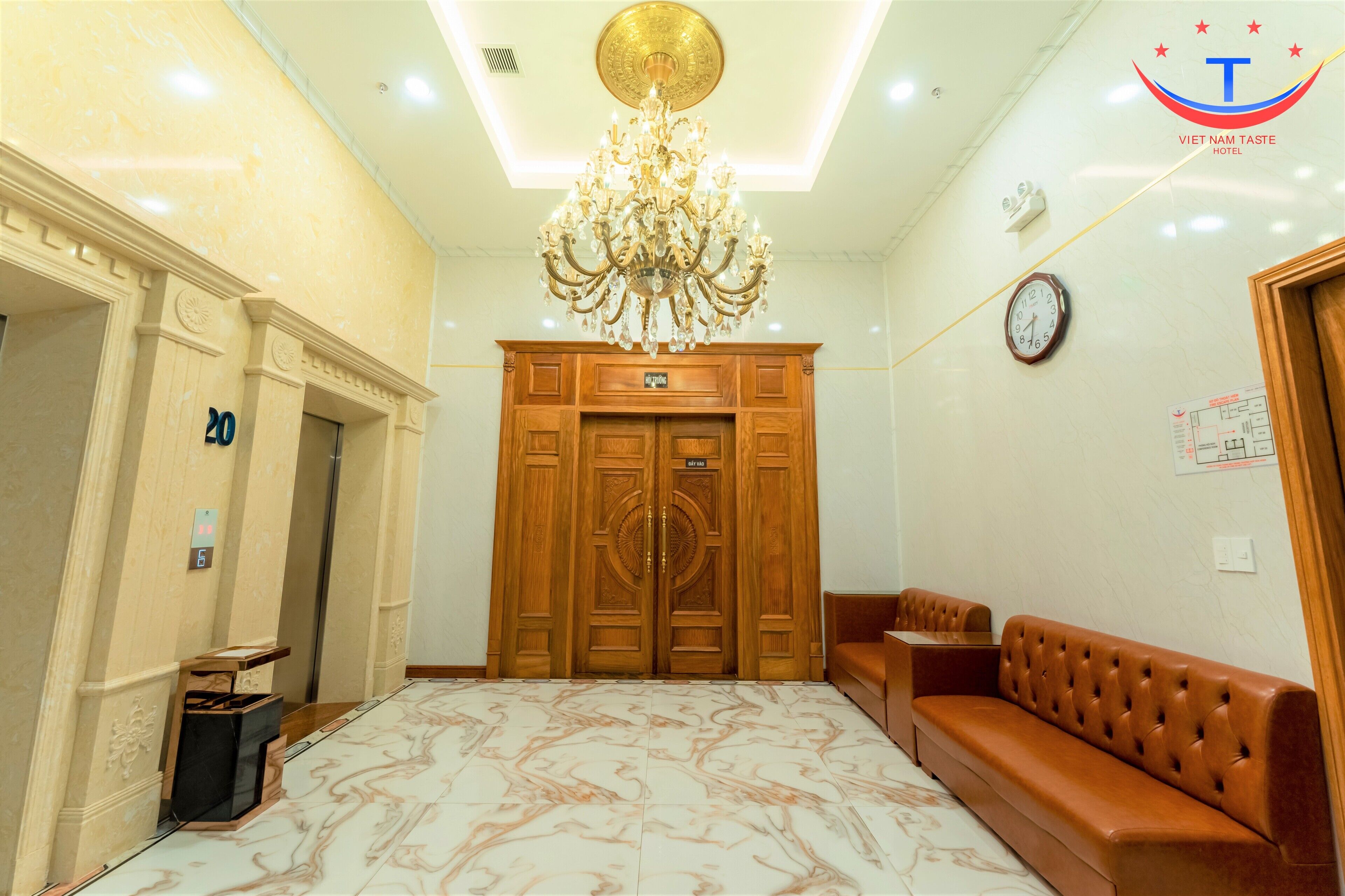Un atrio di hotel con pavimento in marmo, un lampadario, una porta in legno, un orologio e una zona salotto.