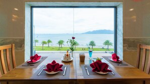 A dining table set for two with a view of the sea and palm trees. - Vietnam Taste Hotel Quy Nhon - Beachfront (Quy Nhon)