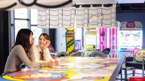 A brightly lit indoor space with a large, colorful table and arcade games in the background.