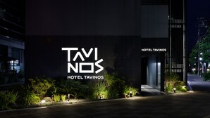 A modern building with a prominent sign for 'TAVINOS HOTEL' illuminated at night.