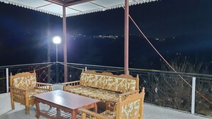 A covered outdoor seating area with a table and two sofas, a railing, and a view of the night sky. - Newly built bnb in a pristine village (Shimla)